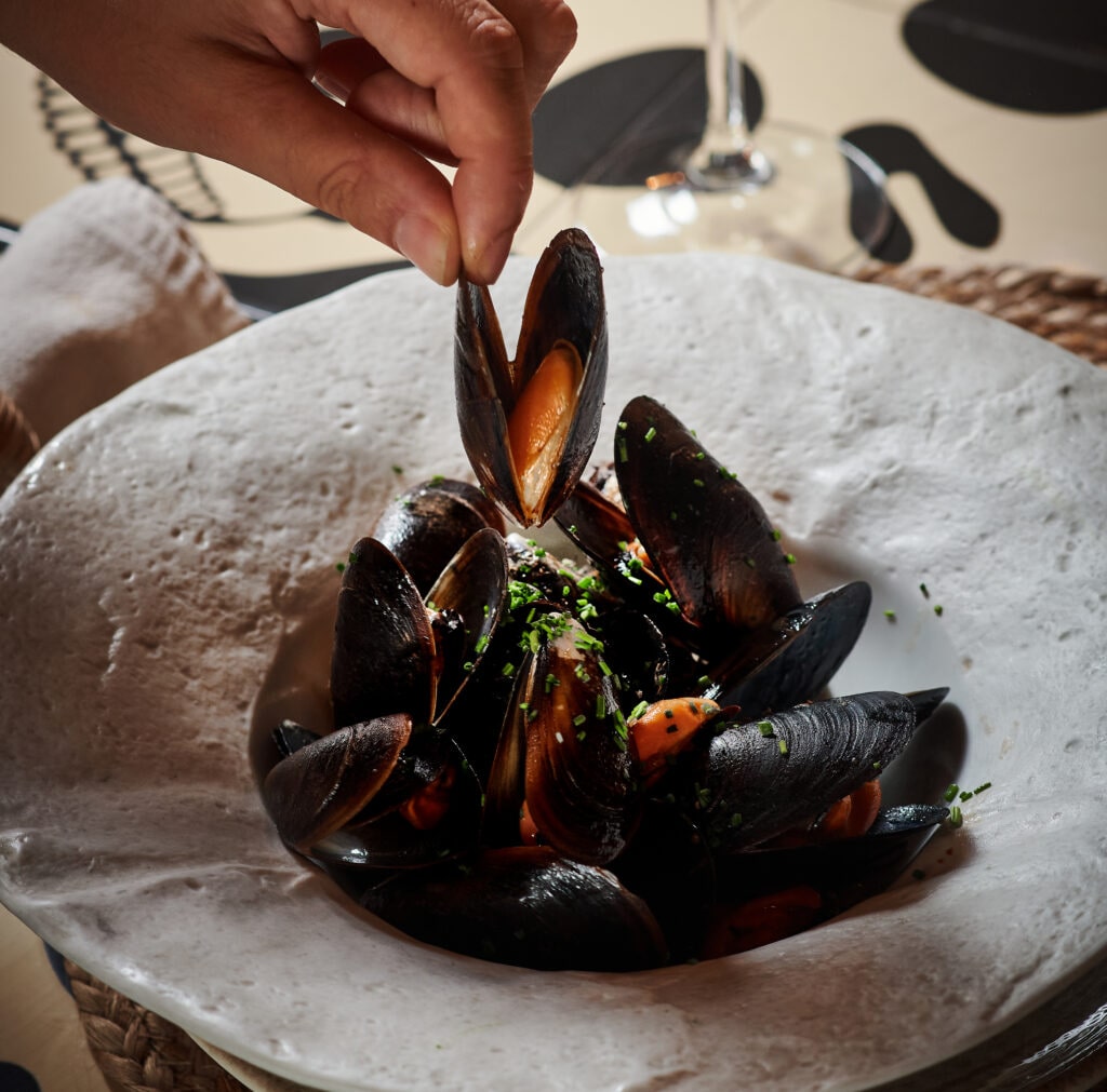 Mano cogiendo un mejillón de un plato de La Mar de Gamberra